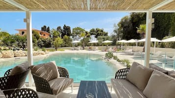 Relax by the serene pool surrounded by lush greenery and shaded by a bamboo pergola.