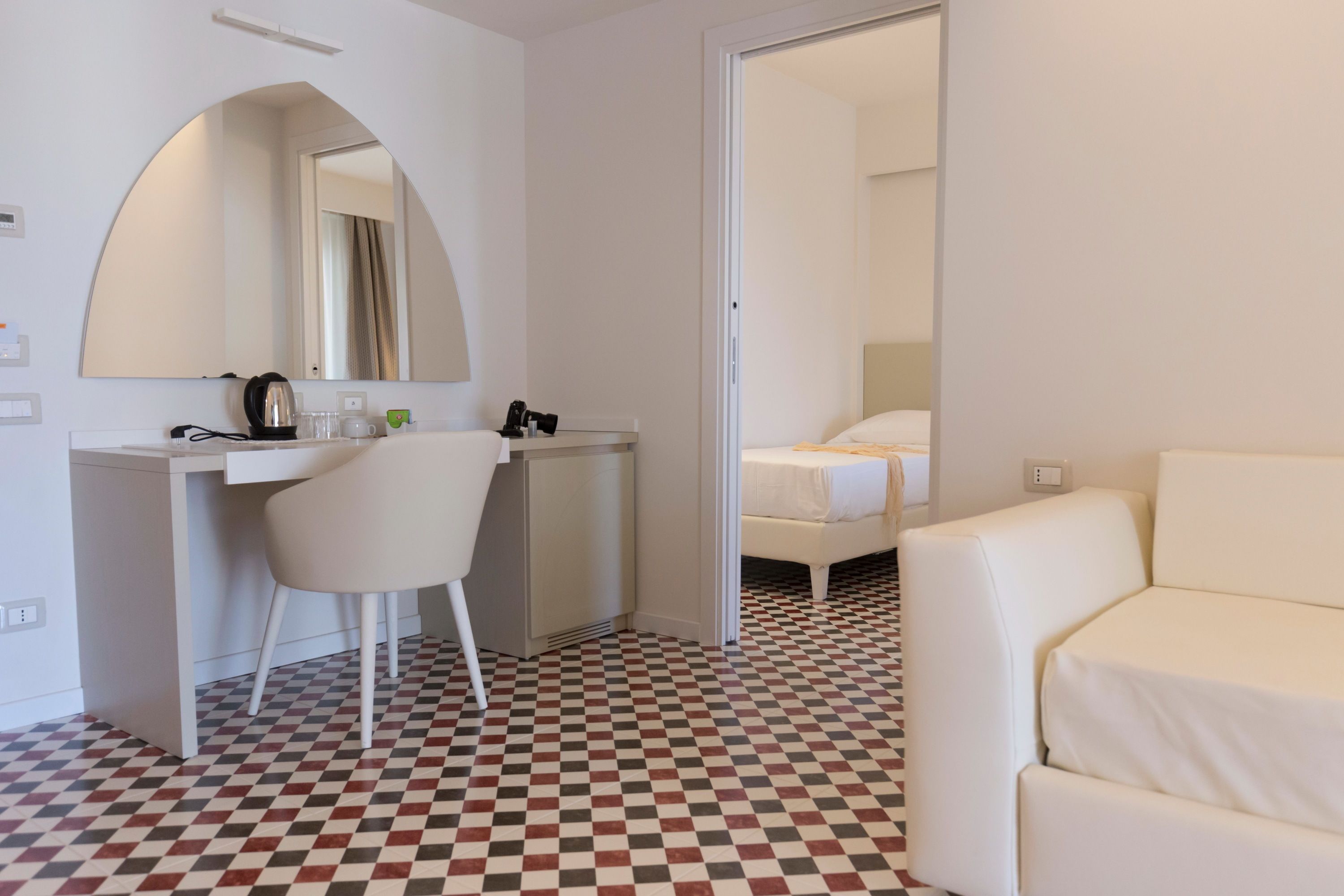 Hotellihuone, jossa on ruutukuviollinen lattia, työpöytä tuolilla, sänky ja suuri peili.