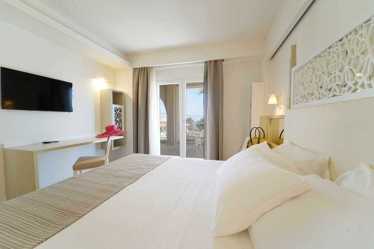 A hotel room with a bed, a desk, a TV, and a view of the outdoors.