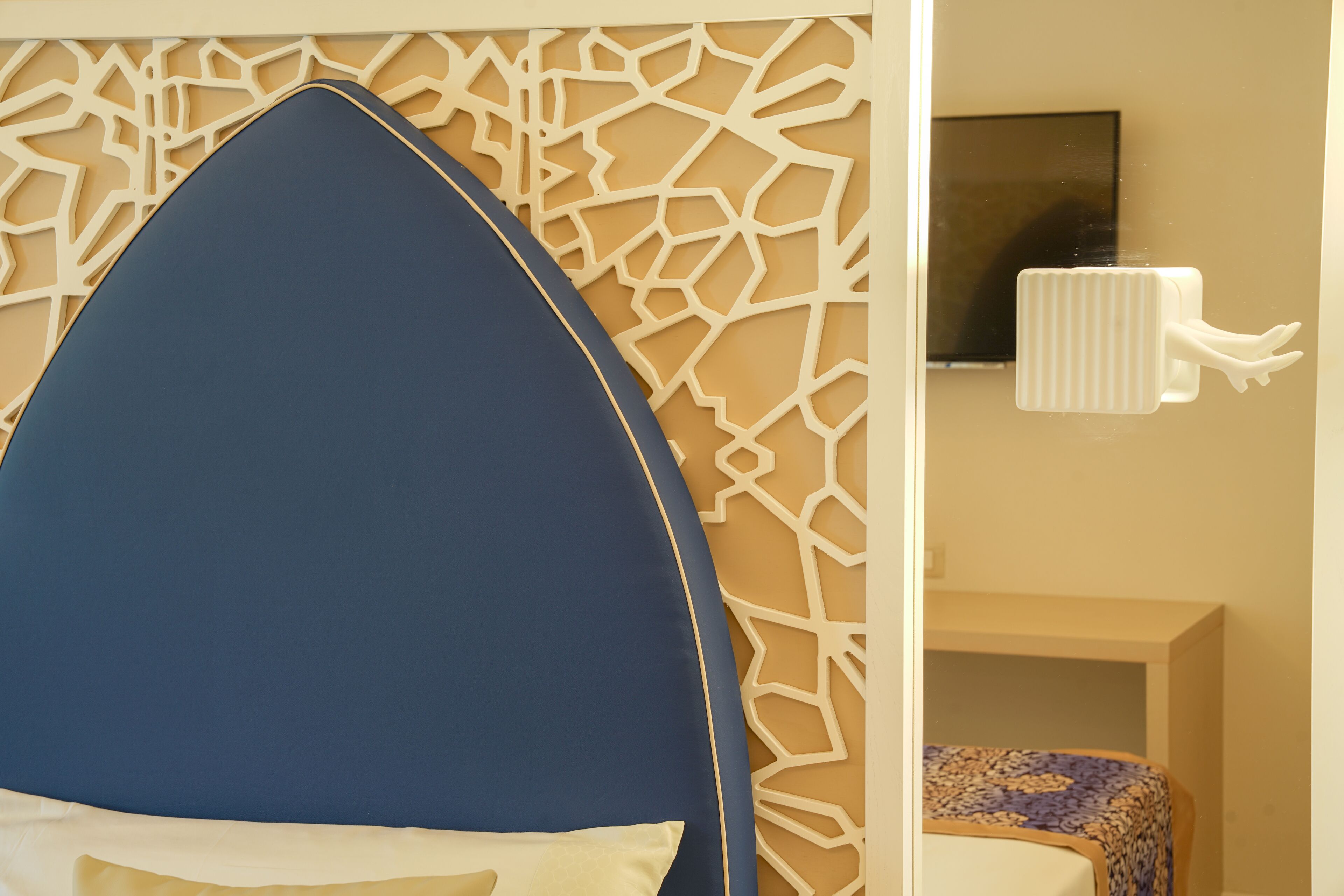 Una habitación moderna con un cabecero azul curvo, un papel tapiz estampado y una mesita de noche pequeña con un cubrecolchón decorativo.