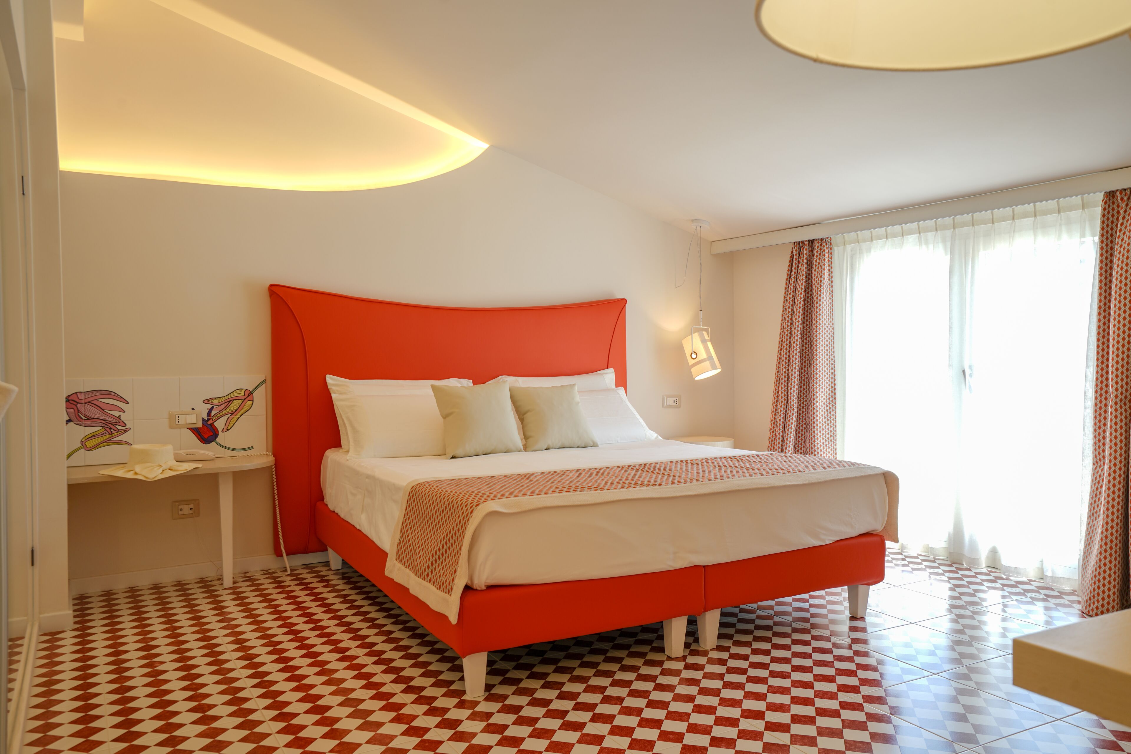 Una habitación de hotel con piso a cuadros, estructura de cama roja y cabecera blanca.