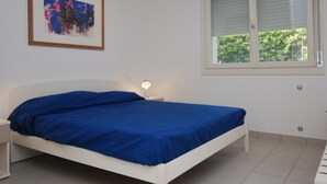 Un dormitorio con una cama individual, una mesita de noche con lámpara, una ventana con persianas y un cuadro en la pared.