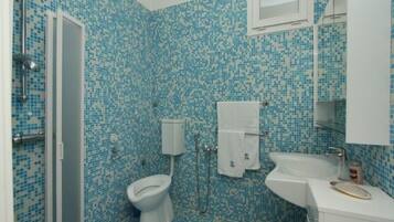 Casa de banho com parede de azulejos mosaicos, sanita, lavatório e chuveiro.
