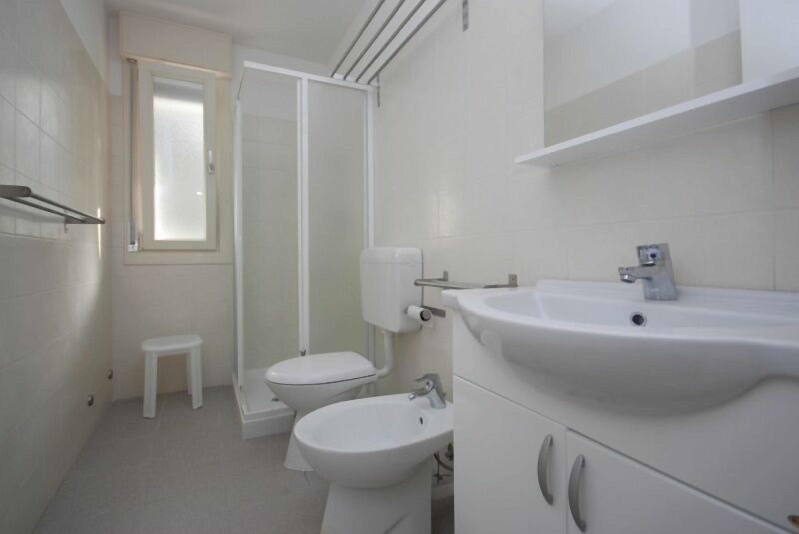 A bathroom with a toilet, bidet, sink, and a small stool.