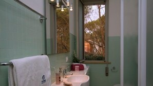 Un baño con lavamanos blanco, un espejo y una ventana con vistas a árboles.