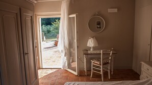 Un dormitorio con cama, escritorio con silla, espejo y puerta abierta que da a un jardín.