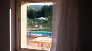 Una ventana con vistas a una piscina, mobiliario exterior y zonas verdes.