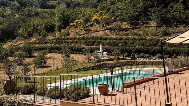 Zona de piscina con valla perimetral, jardines en terrazas y vistas a una colina con árboles y arbustos.