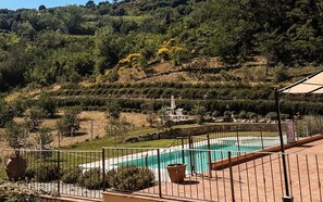 A pool area with a surrounding fence, terraced landscaping, and a view of a hillside with trees and shrubs. - Mulino Della Rivolta (Collesalvetti)