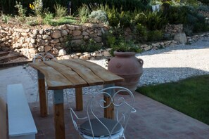 An outdoor patio with a wooden table and metal chairs, a large terracotta pot, and a stone wall in the background. - Mulino Della Rivolta (Collesalvetti)