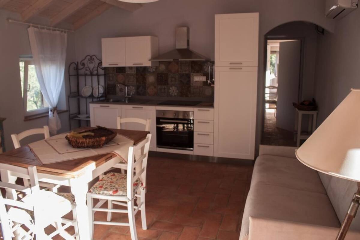 A compact kitchen with white cabinets, a tiled backsplash, and a built-in oven. There is a dining table with chairs and a bench.