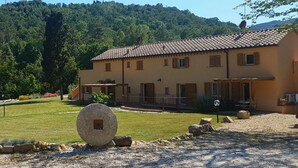 Un edificio de dos pisos con techo de tejas, barandilla de piedra y camino de entrada de grava.