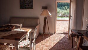 Un cuarto acogedor con sofá, una mesa y una lámpara. Hay un cuadro en la pared y vistas del exterior a través de una puerta.