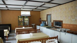 A restaurant with wooden tables and chairs, a counter with plates and glasses, and a refrigerator with beverages.