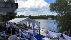 An outdoor event area with tables and chairs, a tent, and a lake view.