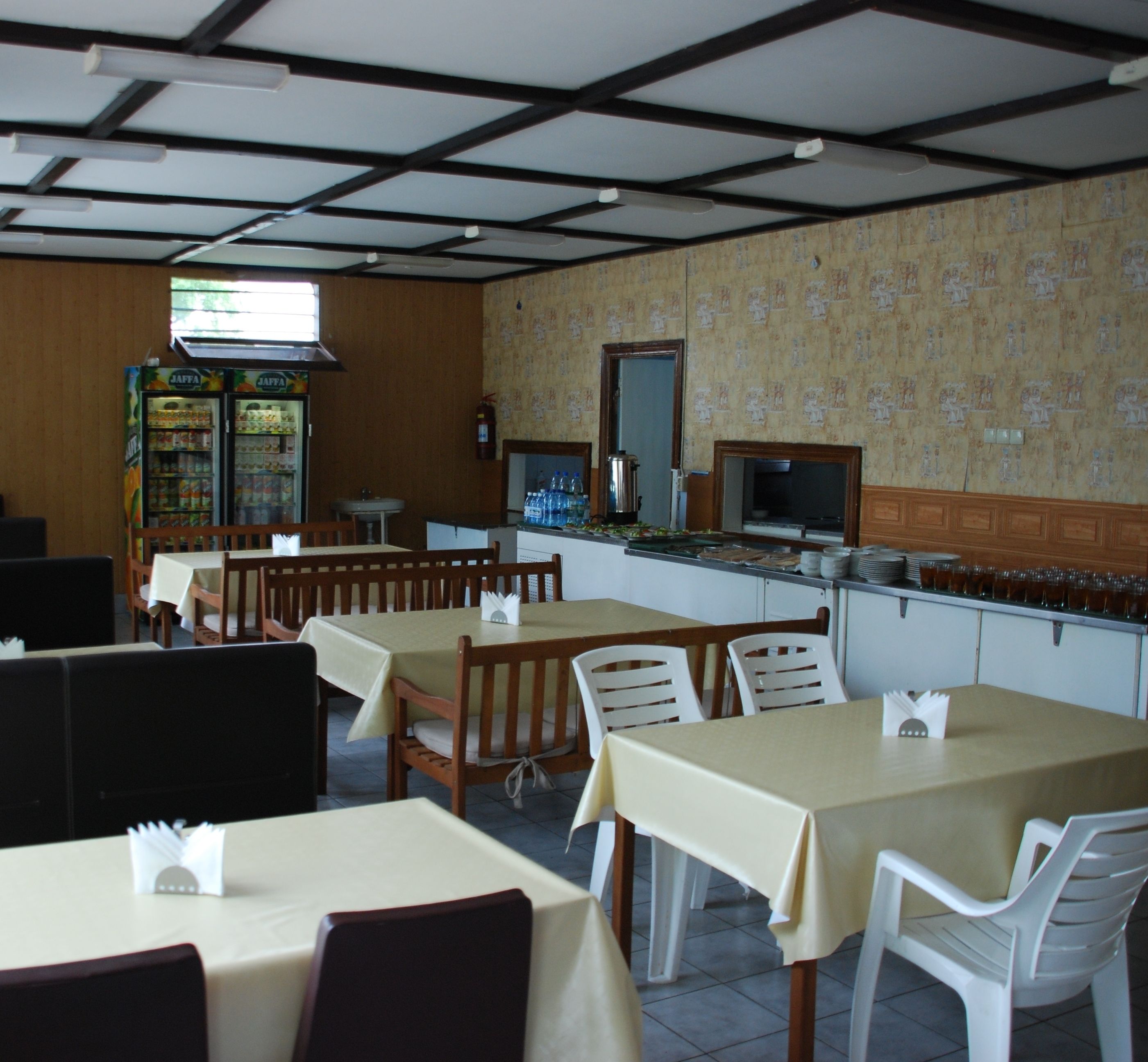 A restaurant with wooden tables and chairs, a counter with a beverage dispenser, and a patterned wall.