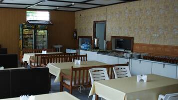 A restaurant with wooden tables and chairs, a counter with a beverage dispenser, and a patterned wall.