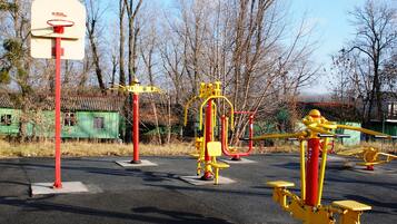 A playground with a basketball hoop, exercise equipment, and a green building in the background.