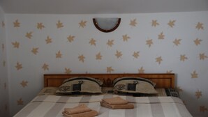 A hotel room with a bed featuring striped bedding, two pillows with embroidered designs, and a headboard with a mirror.