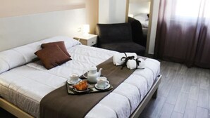 Habitación de hotel con una cama bien hecha, una bandeja con artículos de desayuno, una mesita de noche con lámpara y un espejo en la pared.
