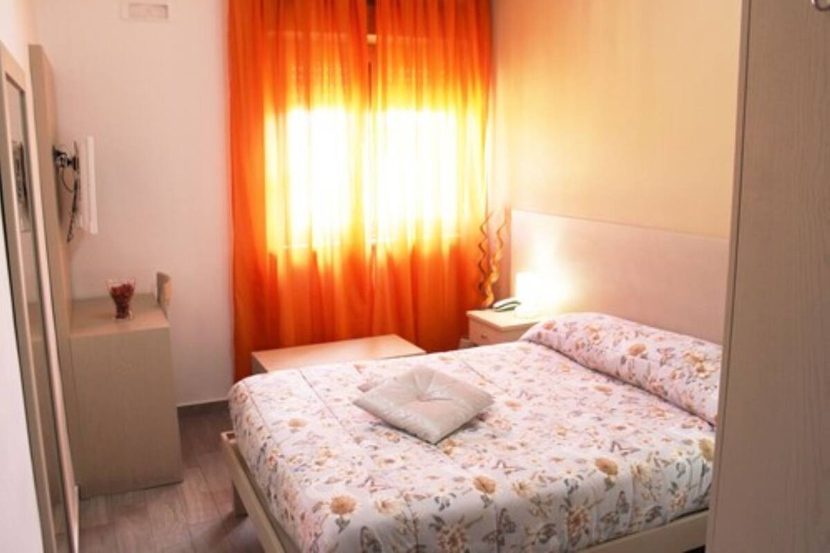 A bedroom with a bed, a nightstand, and a window with orange curtains.