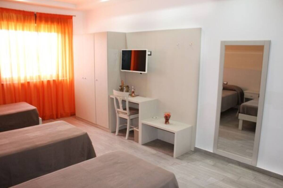 A hotel room with two beds, a desk, a chair, a TV, and a wardrobe.