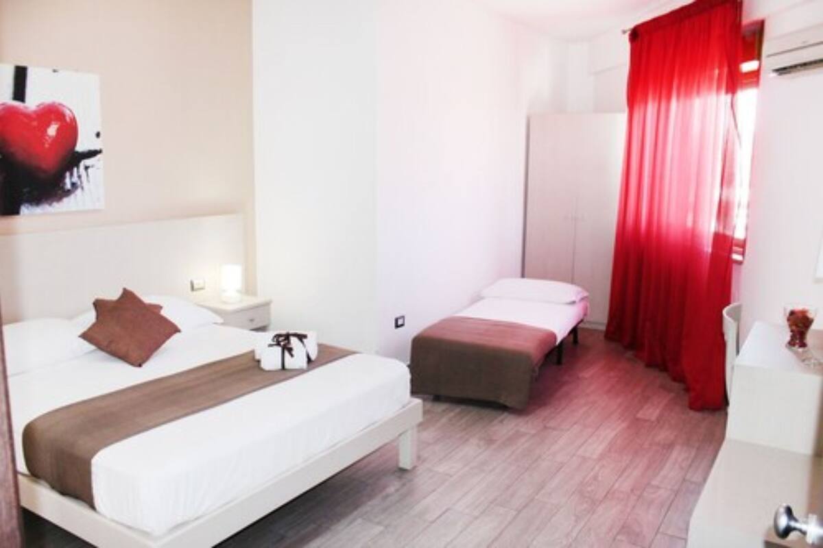 A hotel room with a large bed, a smaller bed, a nightstand, a dresser, and a red curtain.