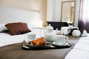 Ein ordentlich gedeckter Frühstückswagen auf einem Bett, mit einem Kopfkissen, einem Teekessel, Tassen und einem Croissant.