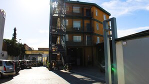 Un edificio de varios pisos con escaleras de emergencia, coches aparcados y una fachada visible.