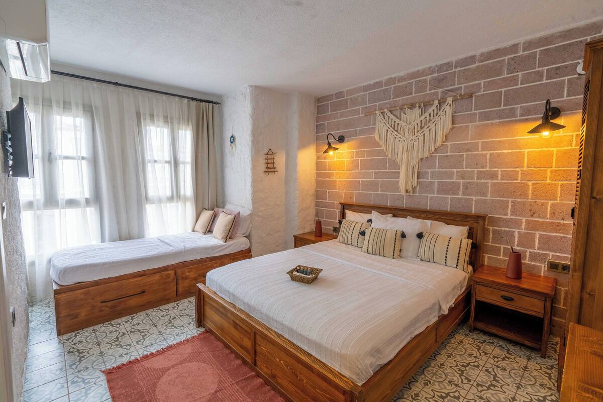 A bedroom with two beds, a brick wall, and a macrame wall hanging.
