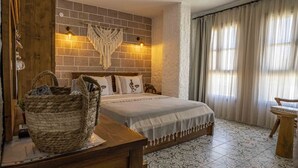Un dormitorio con pared de ladrillo, un colgador de macramé, una cama con edredón estampado, una mesita de noche de madera y un ventanal con cortinas.