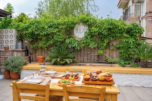 An outdoor dining area with wooden tables and chairs, surrounded by lush greenery and a bamboo fence. - Ajlan Hotel Cunda (Ayvalik)