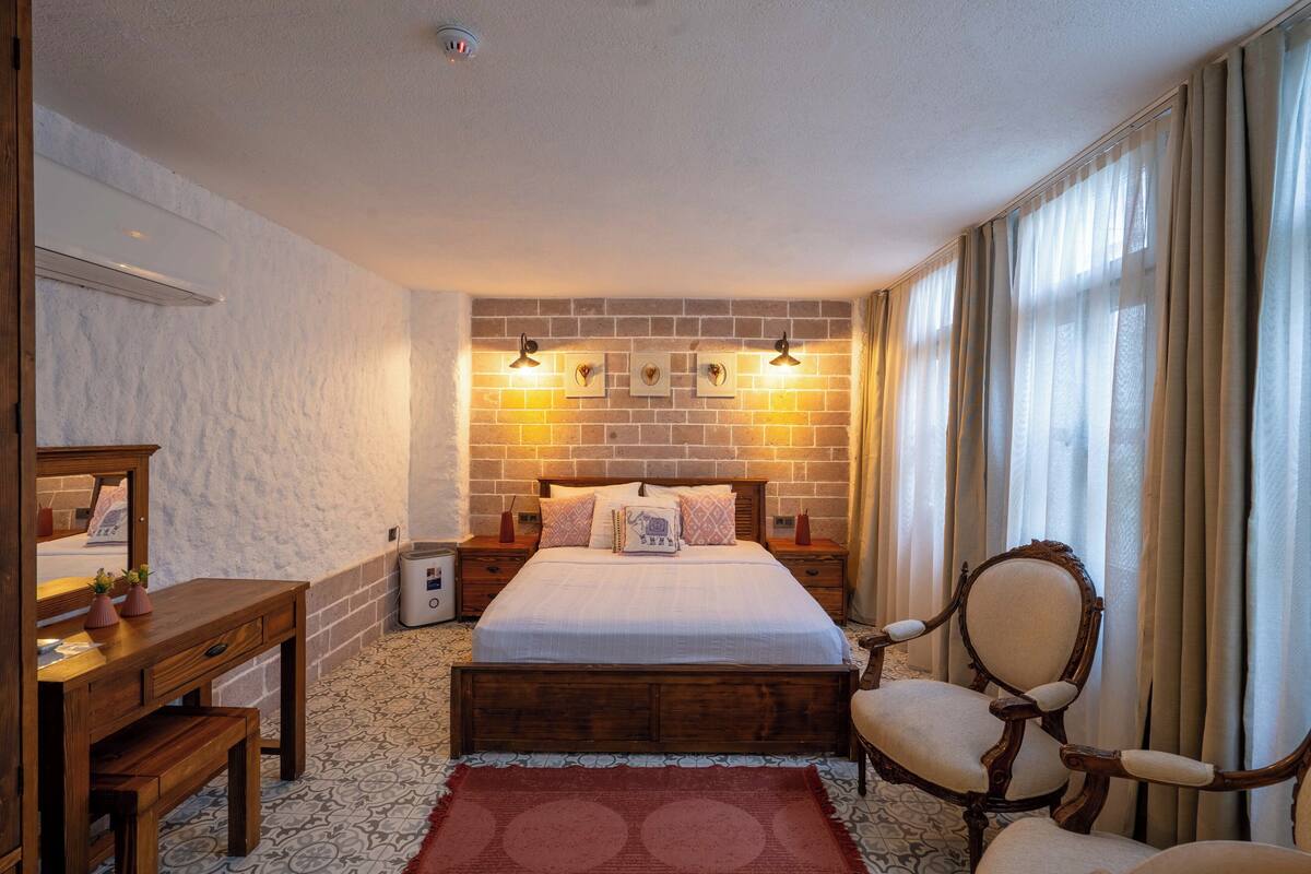A bedroom with a brick-patterned headboard, a wooden bed, a desk with a mirror, and a chair.