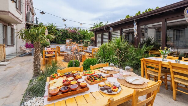 Un espacio de comedor al aire libre con diversos alimentos y bebidas, mobiliario de madera y un entorno de jardín.