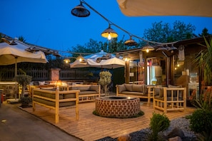 An outdoor patio area with wooden furniture, a brick fire pit, and string lights. - Ajlan Hotel Cunda (Ayvalik)
