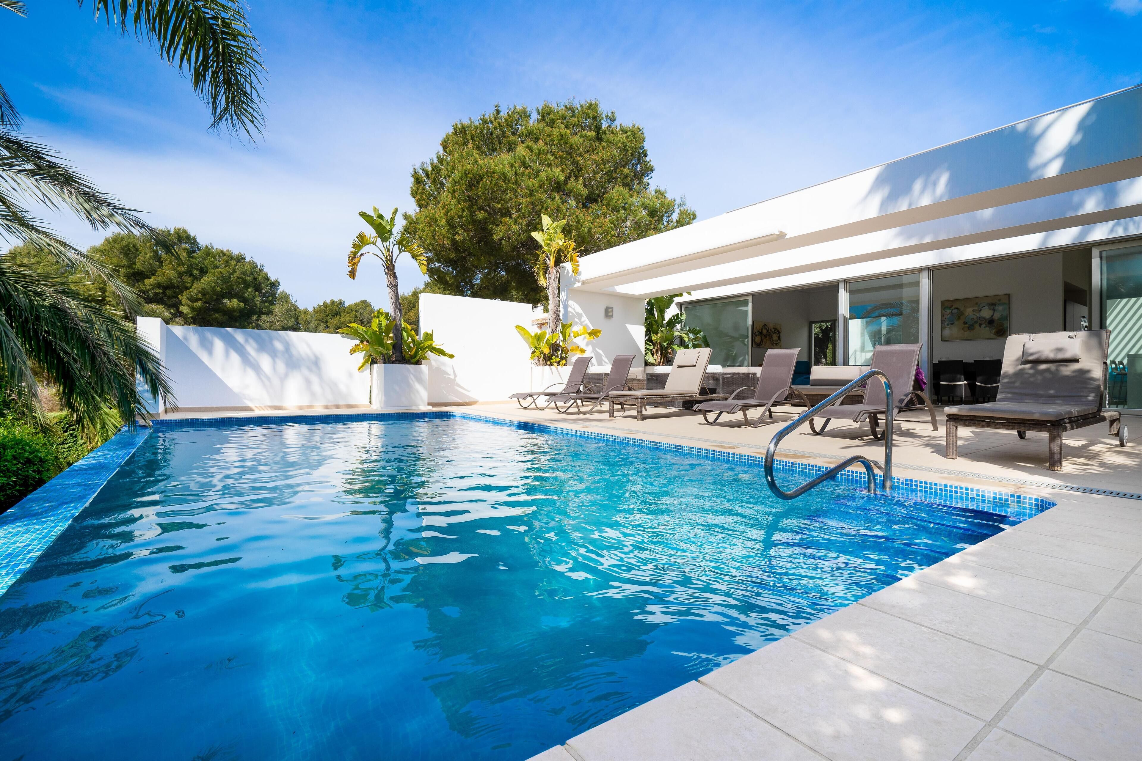A modern outdoor swimming pool with lounge chairs and a white building in the background.