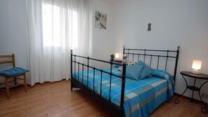 A bedroom with a bed, a chair, a bedside table, and a lamp.
