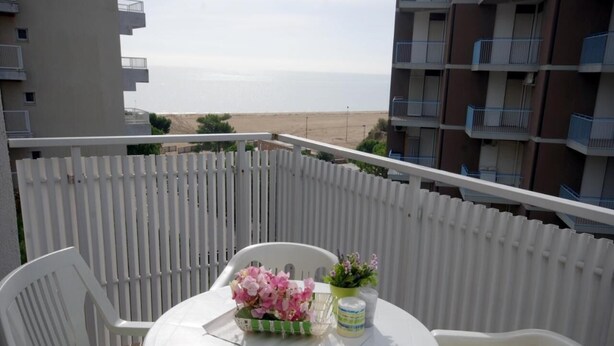A balcony with a round table and two chairs, a flower arrangement, and a potted plant.