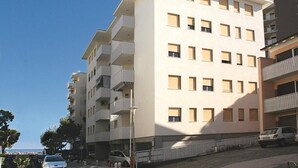 A multi-story residential building with balconies, a parking area, and a clear sky.