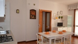 A compact kitchen with a gas stove, a dining table with orange chairs, and a TV on a cabinet.