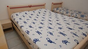 A bedroom with two single beds, each with a patterned bedspread. There is a small bedside table and a drawer under each bed. - Arcobaleno (Lignano Sabbiadoro)