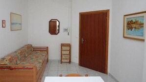 A room with a wooden bed, a wooden side table, a small wooden cabinet, and a wooden door. - Arcobaleno (Lignano Sabbiadoro)