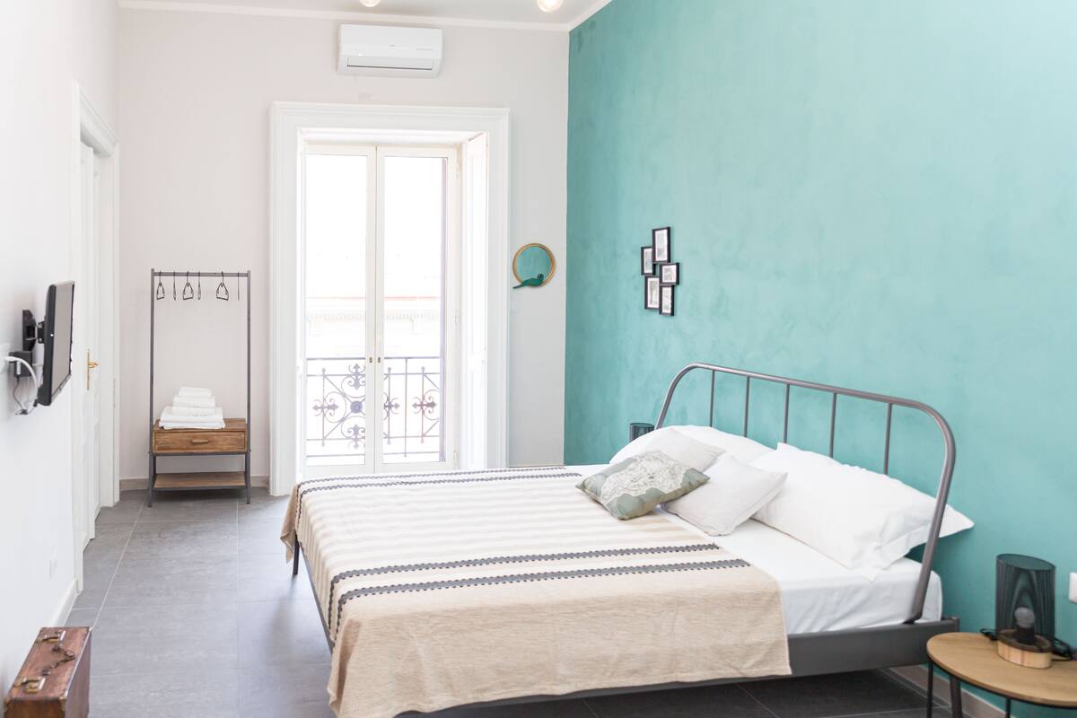A bedroom with a bed, a bedside table, a mirror, and a door leading to a balcony.
