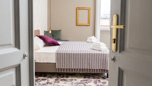 A bedroom with a bed, pillows, a blanket, a hanging light, a framed picture on the wall, and a window. - N'Art Suites Napoli (Naples)