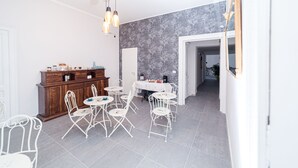 A dining area with white metal chairs and a table, a wooden cabinet, and a gray patterned wall. - N'Art Suites Napoli (Naples)