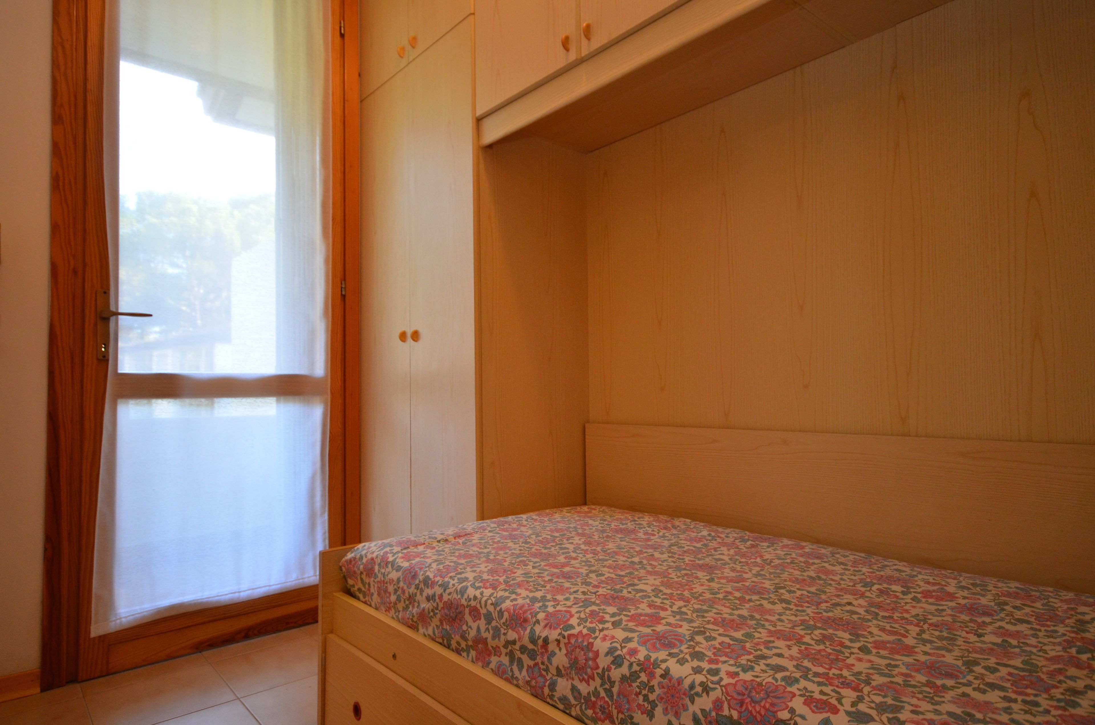 A bedroom with a single bed, wooden wardrobe, and a sliding glass door.