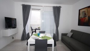 A modern living room with a dining area, a flat-screen TV mounted on the wall, a grey sofa, and a painting on the wall. - Arketipi (Lignano Sabbiadoro)