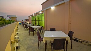 An outdoor dining area with tables and chairs, a concrete floor, and a building with large windows in the background. - Hotel Ali Plaza (Sylhet)