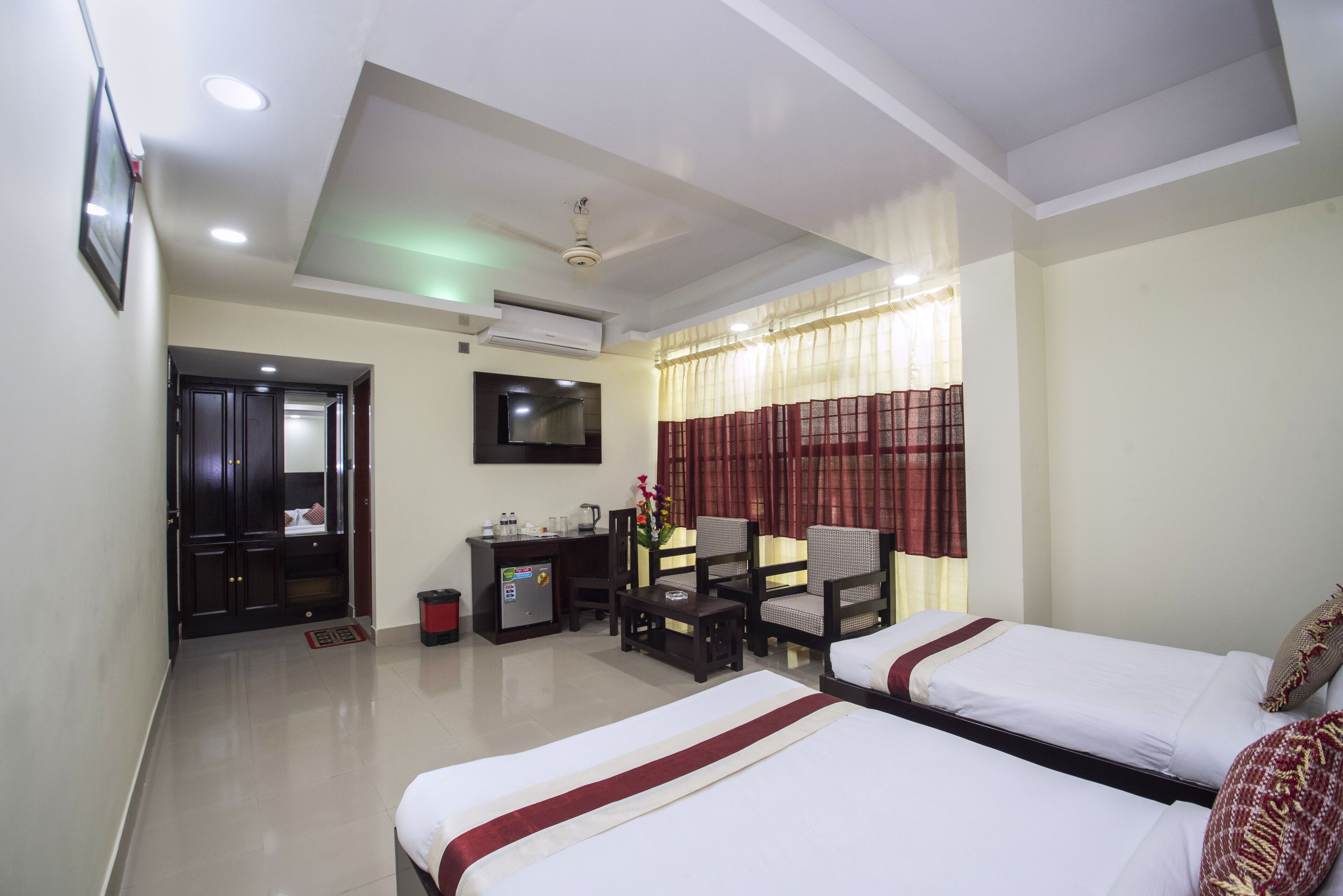A hotel room with two beds, a desk with a chair, a TV, and a window with curtains.