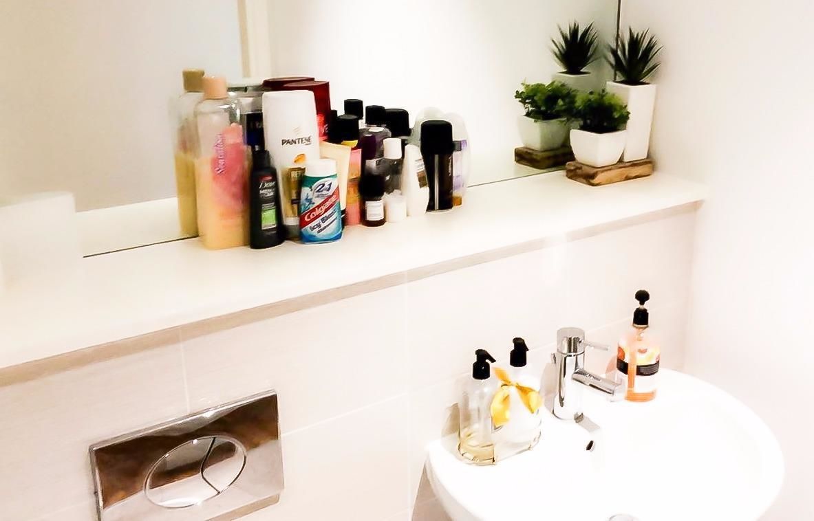 A bathroom with a white sink, two bottles of hand soap, and a variety of toiletries on a shelf above the sink.
